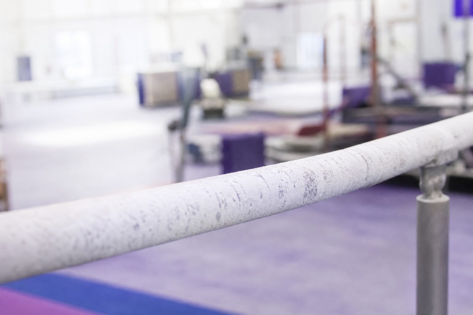 Chalk dust on a bright bar rail with a sunlit gym in the background