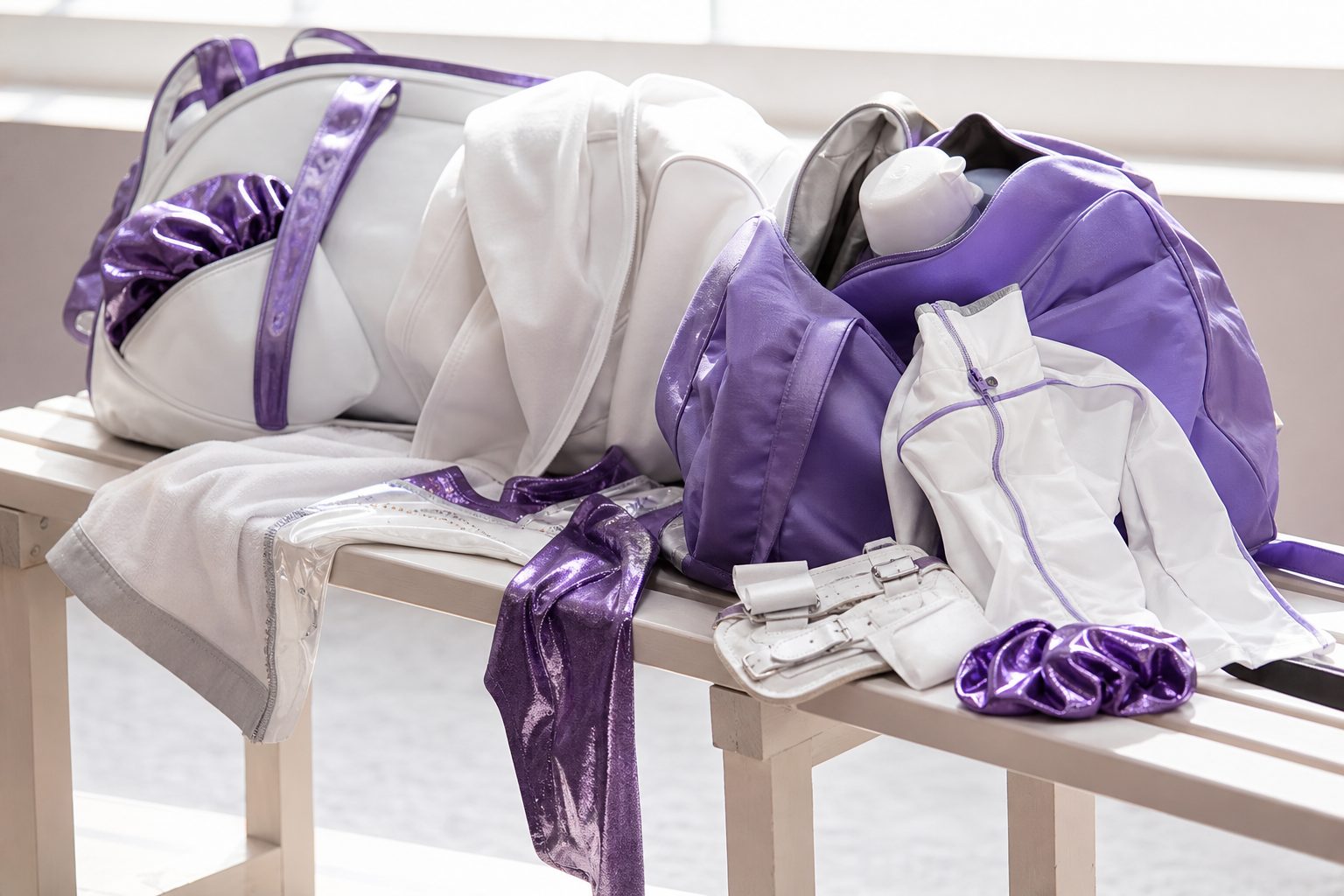 Gym bags, grips and warm up jackets laid out on a pale bench in morning light