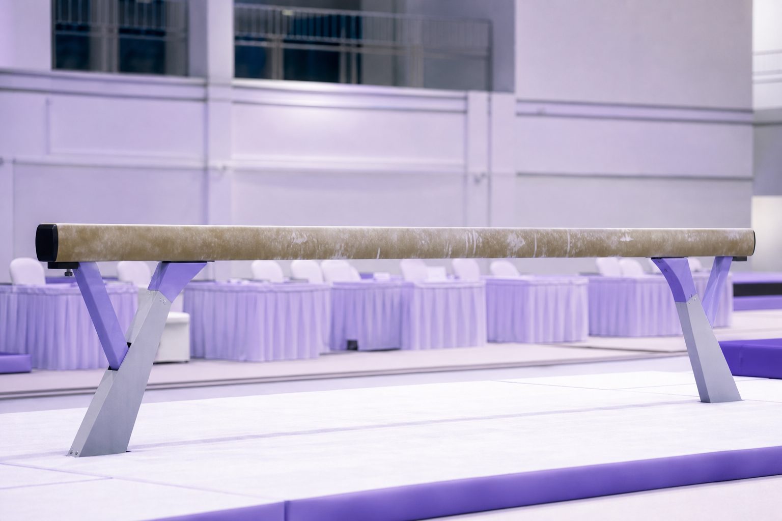Balance beam under bright competition lighting with a judges table in soft focus